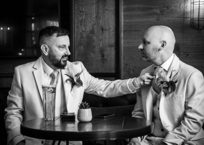 A groom leans in to straighten the other groom's tie during a quiet, candid moment before their Birmingham wedding.